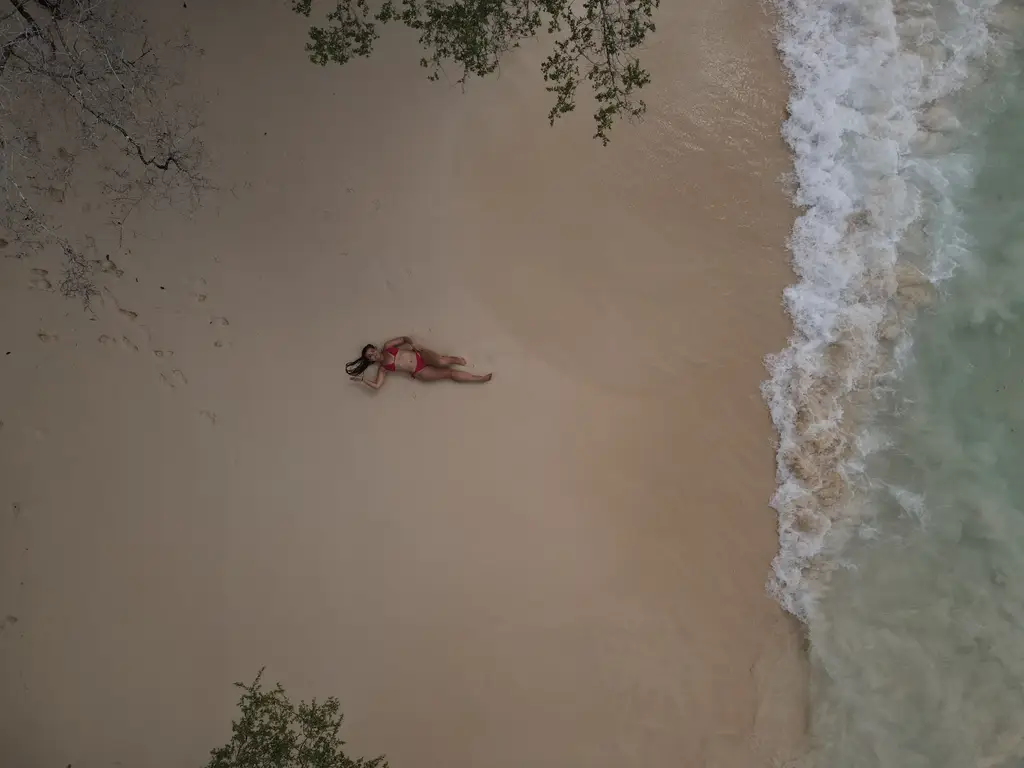 Aerial view looking down at a person lying on wet sand where the surf runs up the beach