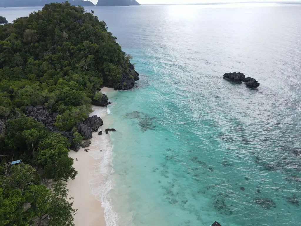 A small bay with black rock at one end, white sand, and clear turquoise water shading to deep blue