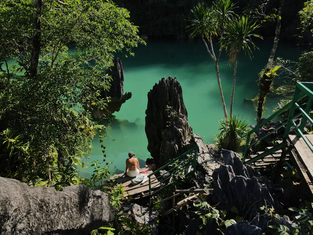 A green lagoon enclosed by karst and jungle, with a wooden viewing platform built onto the rock