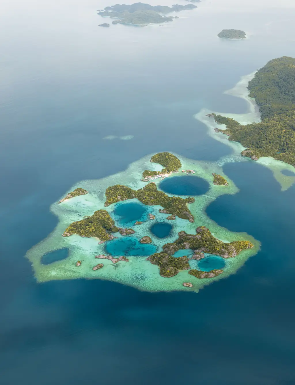Aerial view of a shallow reef platform holding several deep blue pools among low green islets
