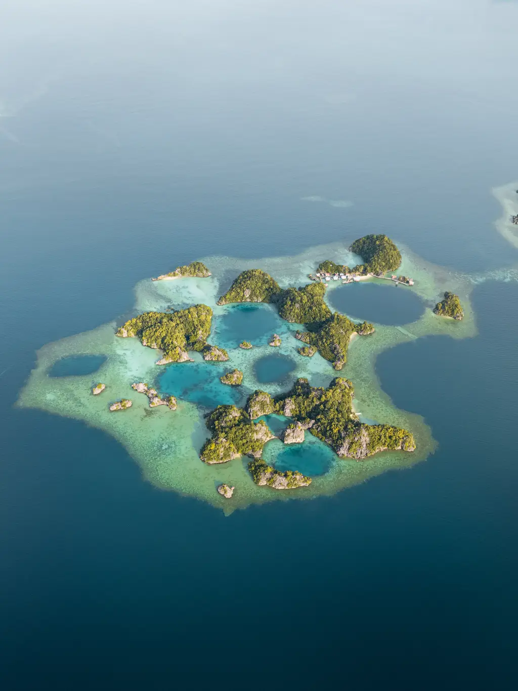 Aerial view of a reef platform enclosing a group of deep blue pools between low green islets
