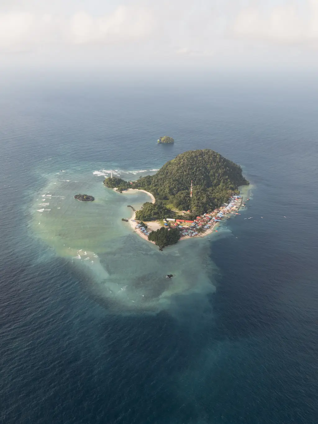 A small island with a dense village along one shore, ringed by shallow reef