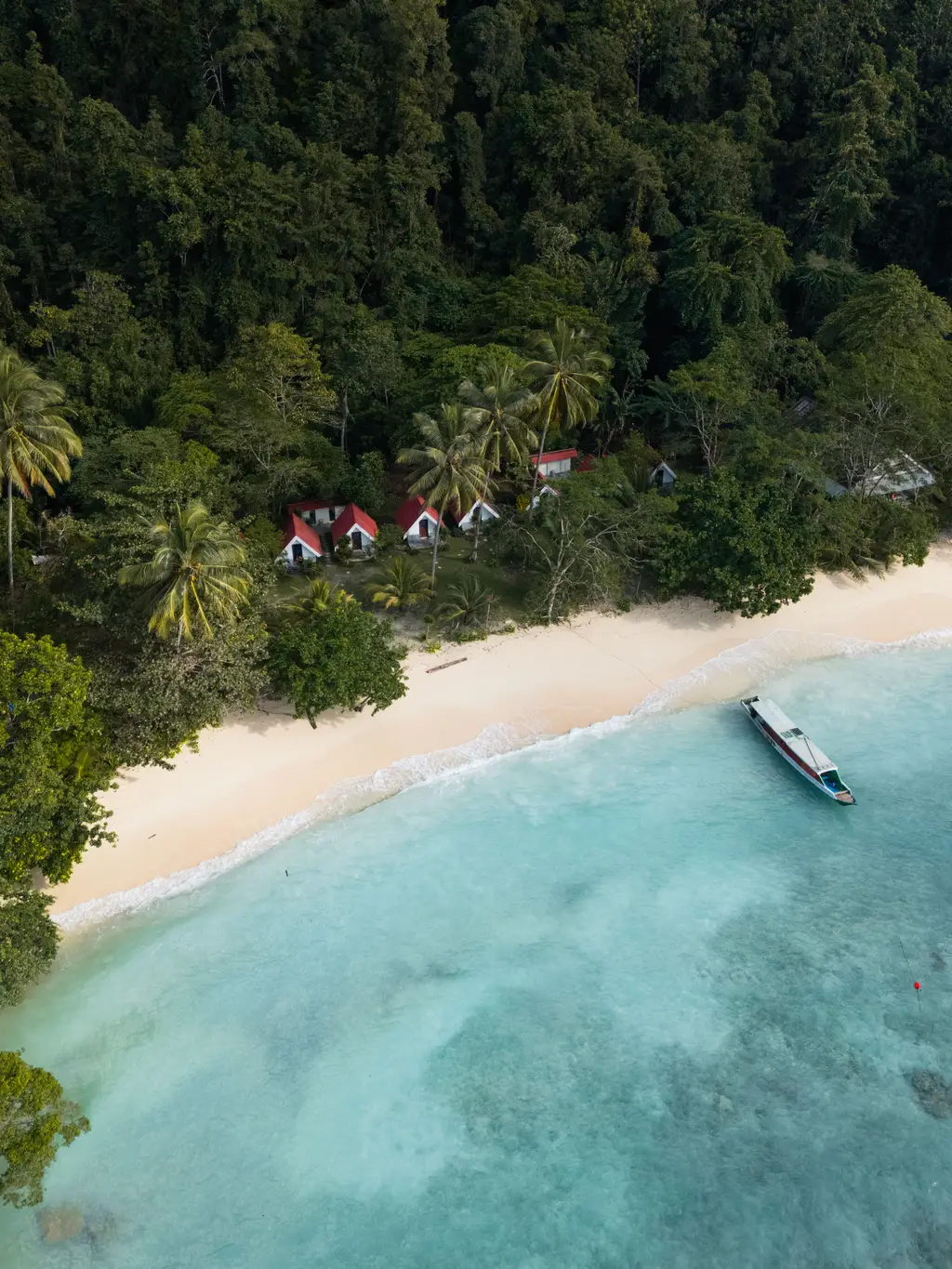 Cottages with red roofs set back from a white sand beach, with a boat moored offshore
