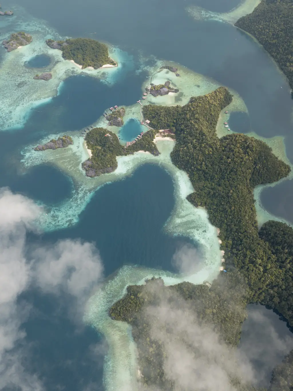 Turquoise shallows and deeper pools among scattered green islets, seen from high above