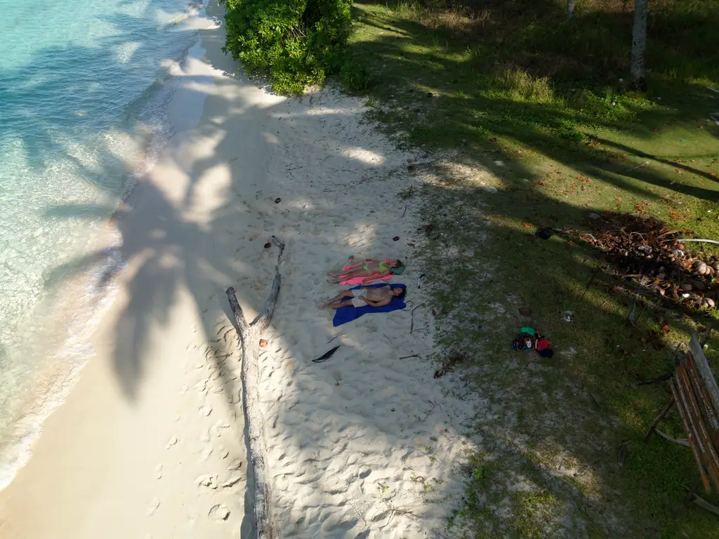 The shadow of a palm falling across bright white sand, with belongings laid out on the beach