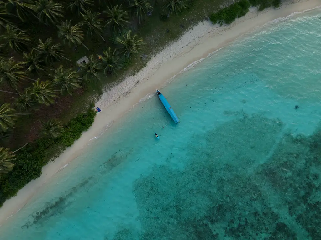 A wooden boat pulled up on a white sand beach beside clear turquoise water