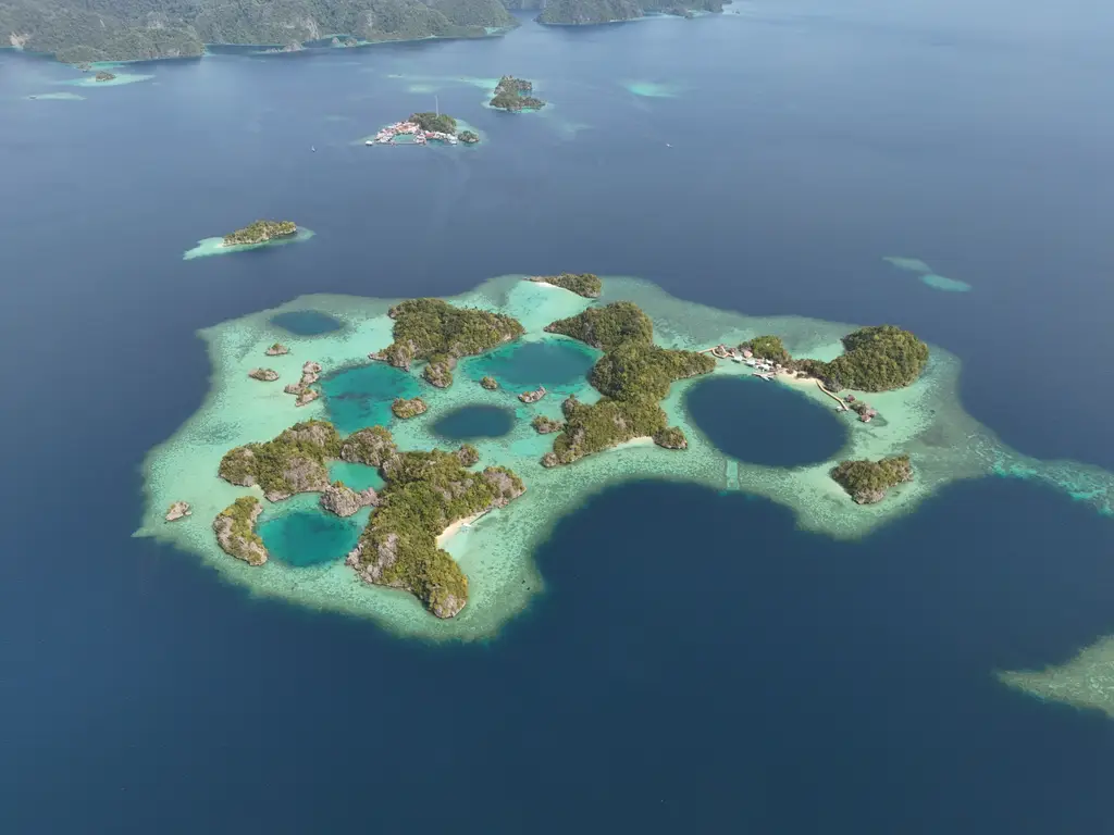 A shallow reef platform holding a dozen deep blue pools between low green islets, ringed by dark open water