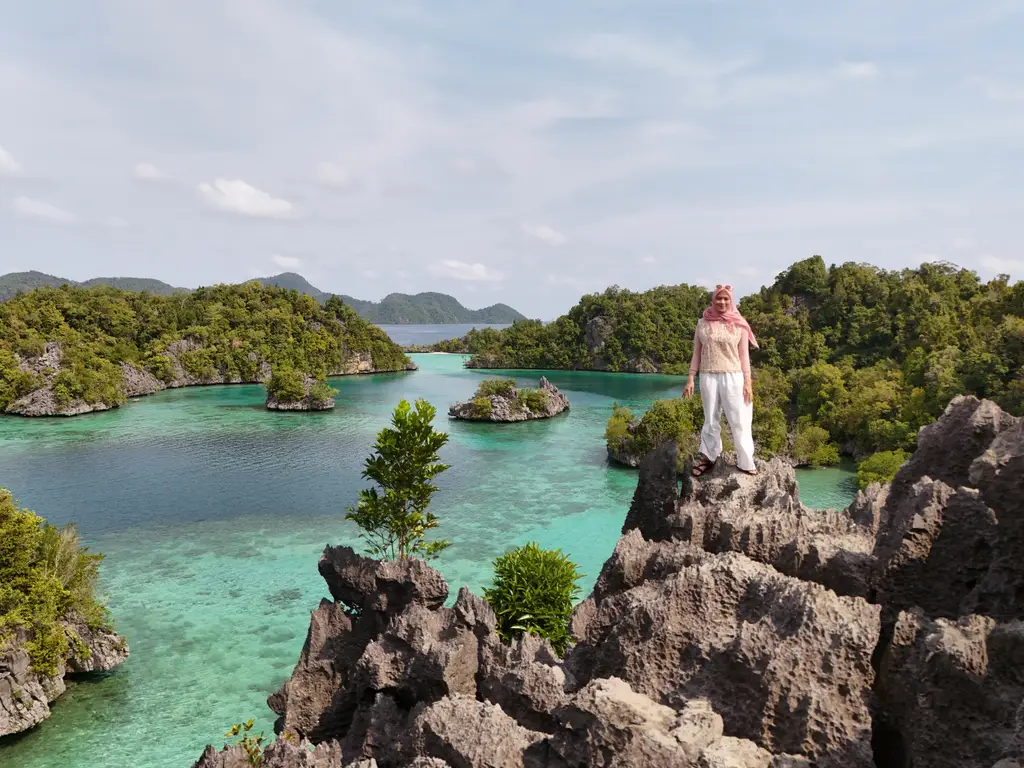 A person standing on a sharp limestone pinnacle looking out over a bay of karst islands