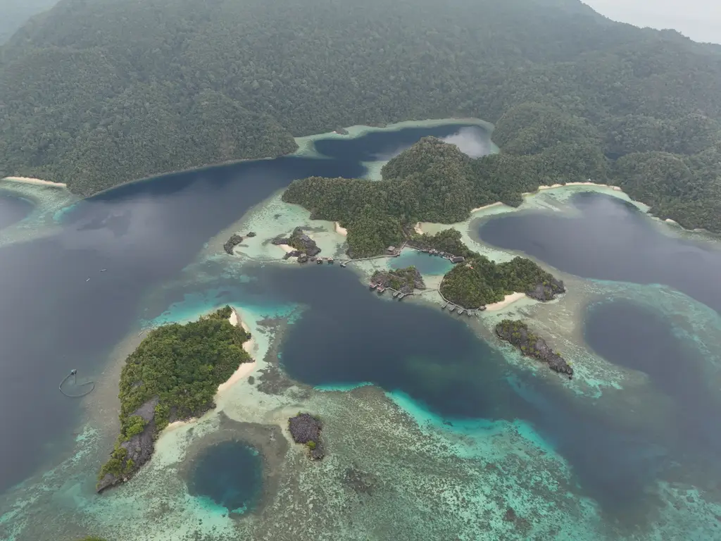 A wide archipelago of green islets in turquoise shallows, with a large forested mountain rising behind it