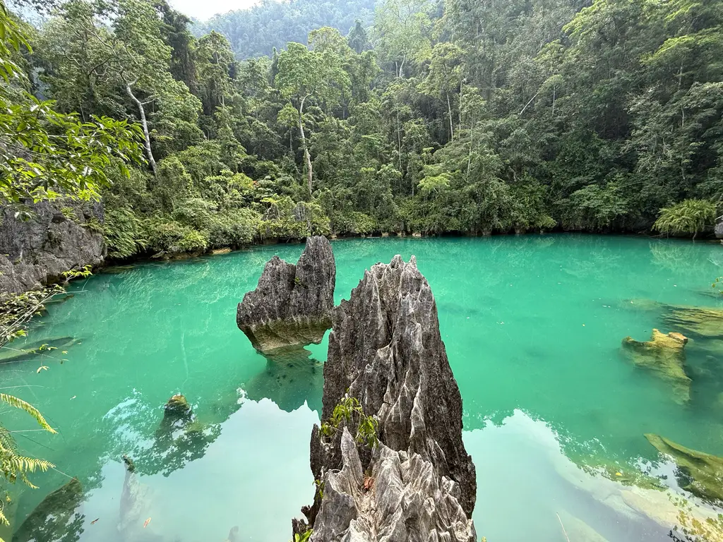 A wave-undercut limestone tower standing in a still green lagoon, its base eaten away at the waterline